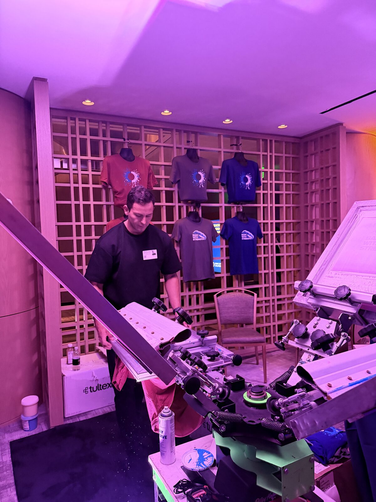 Operator loading a blank shirt onto the screen press at the bar