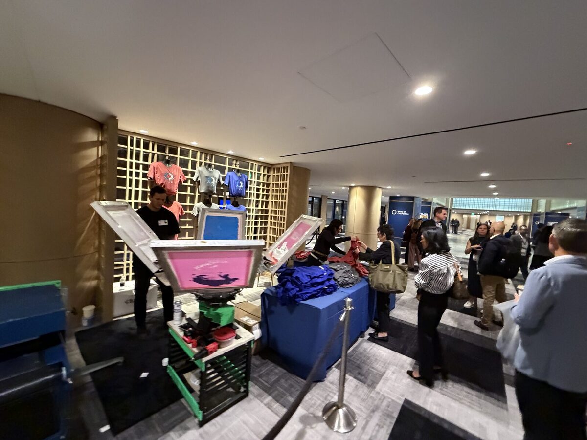 Crowd gathered around the printing station watching a shirt get made